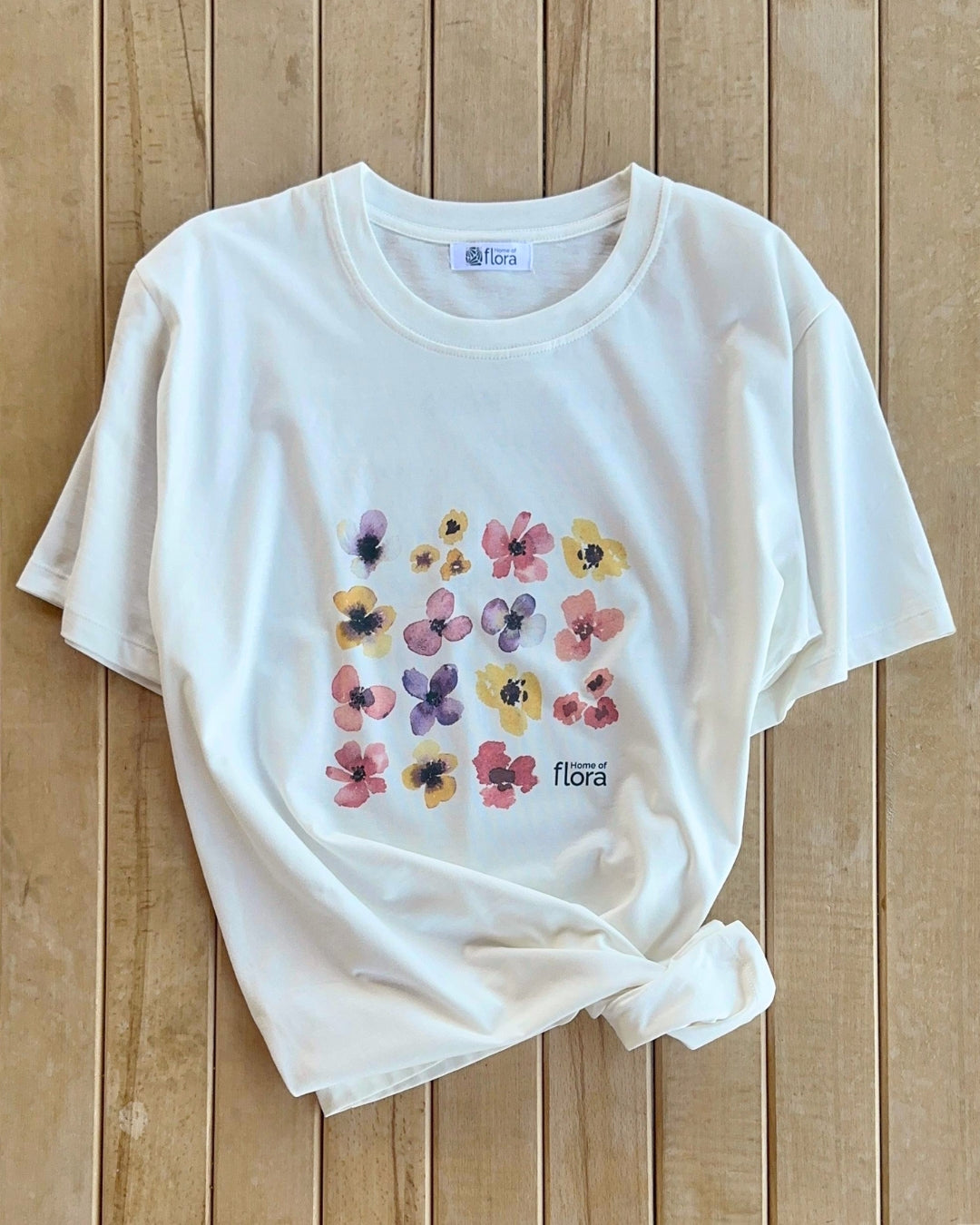 White t-shirt with colorful floral design on a wooden surface