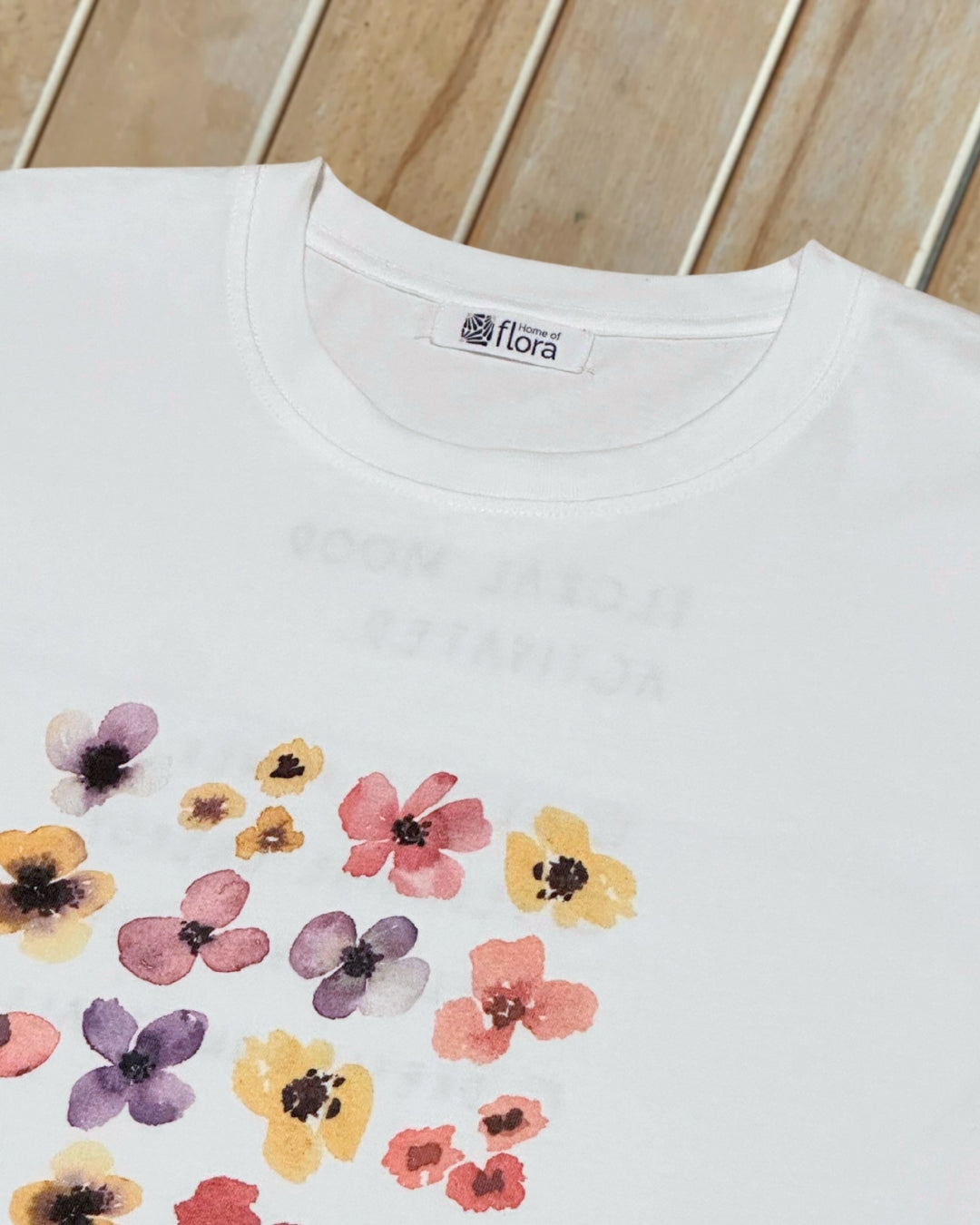 White t-shirt with colorful floral pattern close up, round neck on a wooden surface