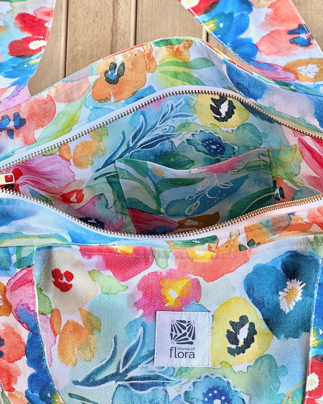 Colorful floral-patterned bags with a visible brand logo on a wooden surface.