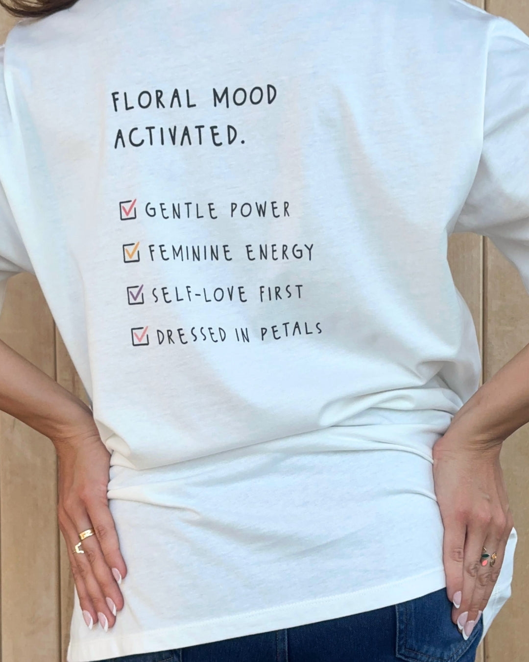 Person wearing a white t-shirt with colorful floral designs and 'House of Flora' text.