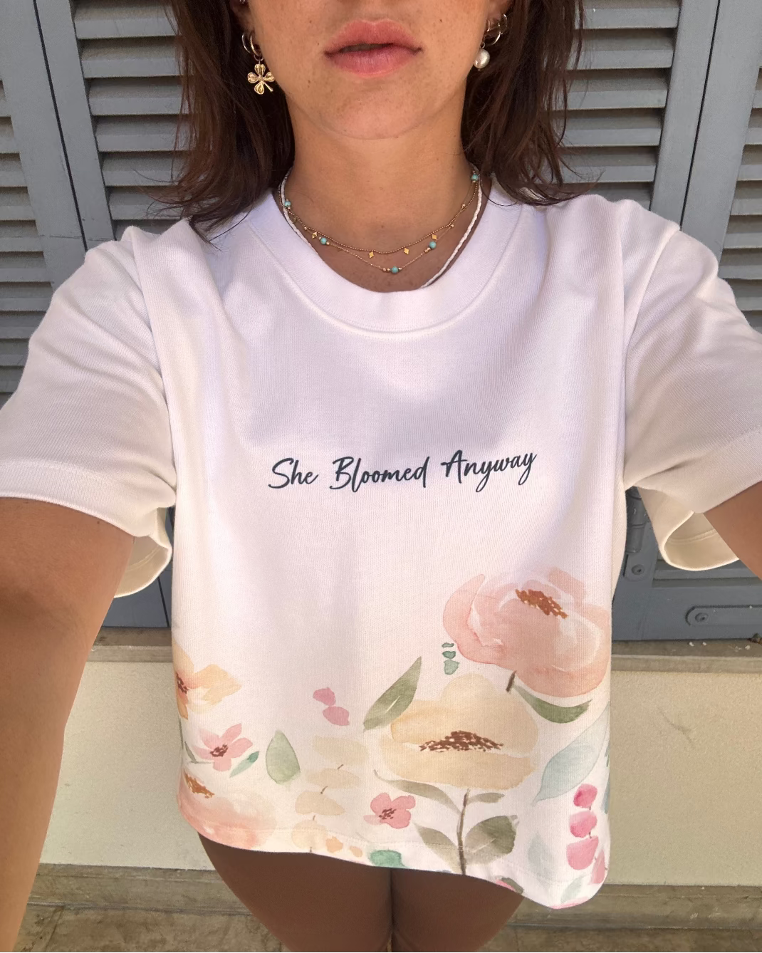 woman wearing a white t-shirt with floral design and text 'She Bloomed Anyway'