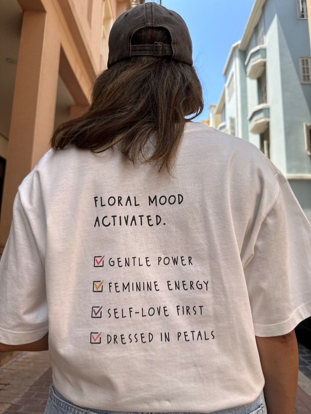 Person wearing a white t-shirt with text on the back, standing outdoors.