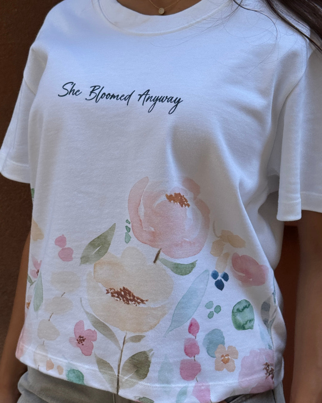 Person wearing a white t-shirt with floral design and text.