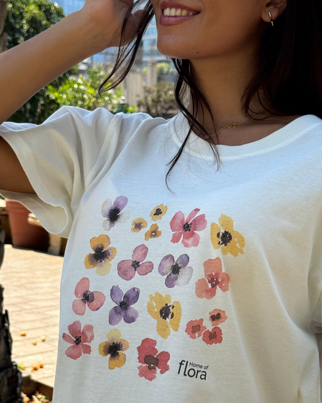 Person wearing a white t-shirt with floral designs and 'flora' branding.