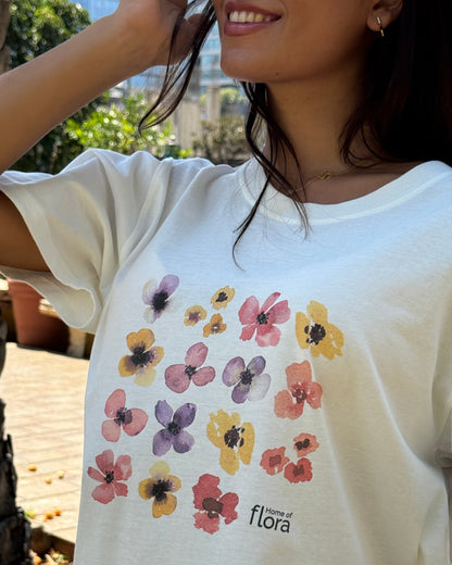 Person wearing a white t-shirt with floral designs and 'flora' branding.