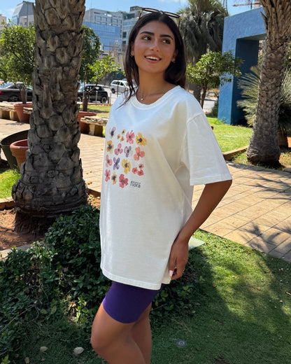 Woman wearing a white t-shirt with colorful graphics in an outdoor setting with palm trees and buildings.