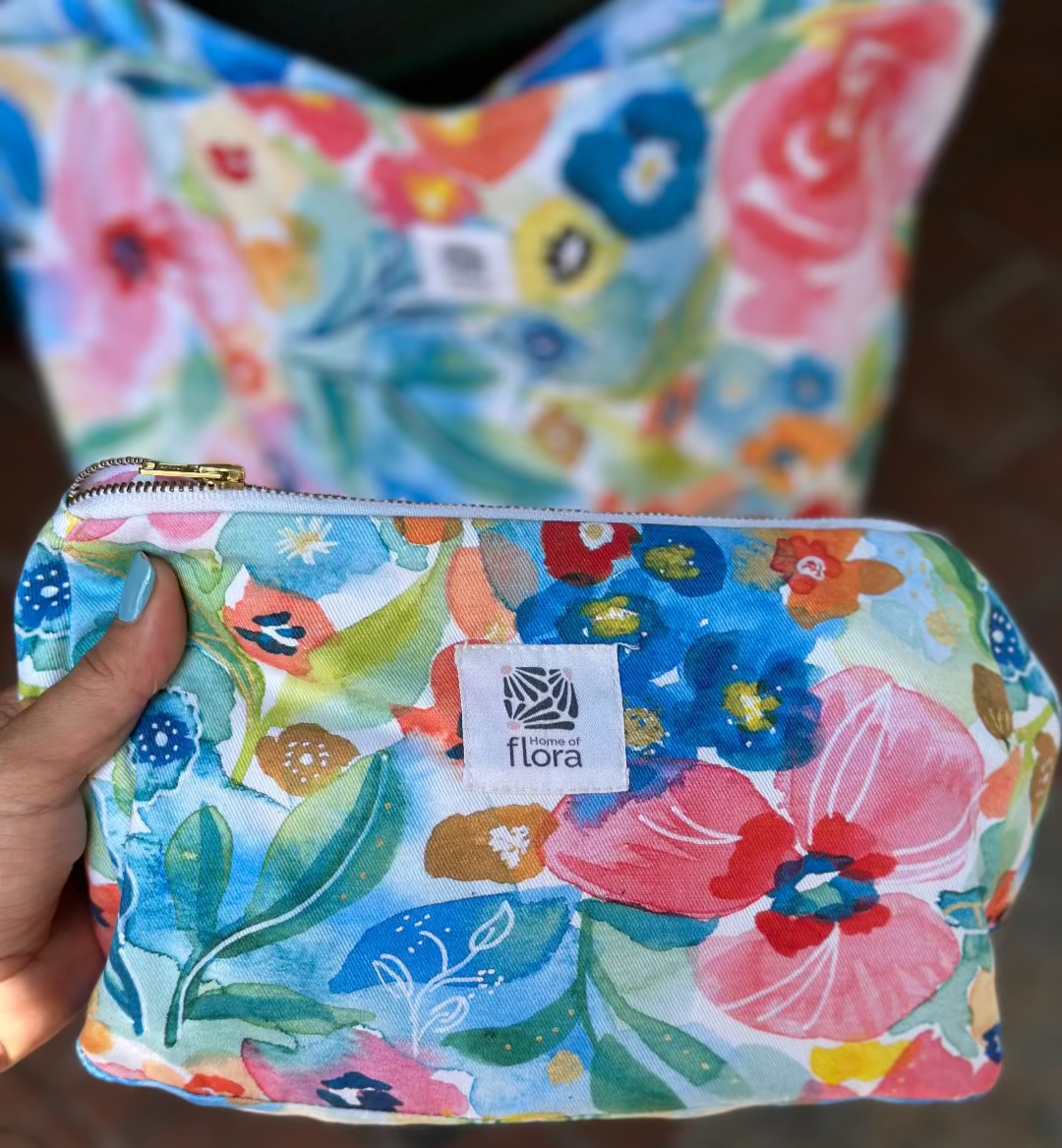 Floral-patterned pouch held by a hand with 'flora' brand label.