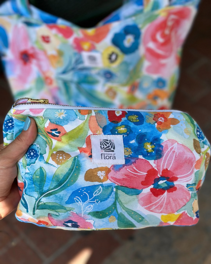 Floral-patterned pouch held by a hand with 'flora' brand label.