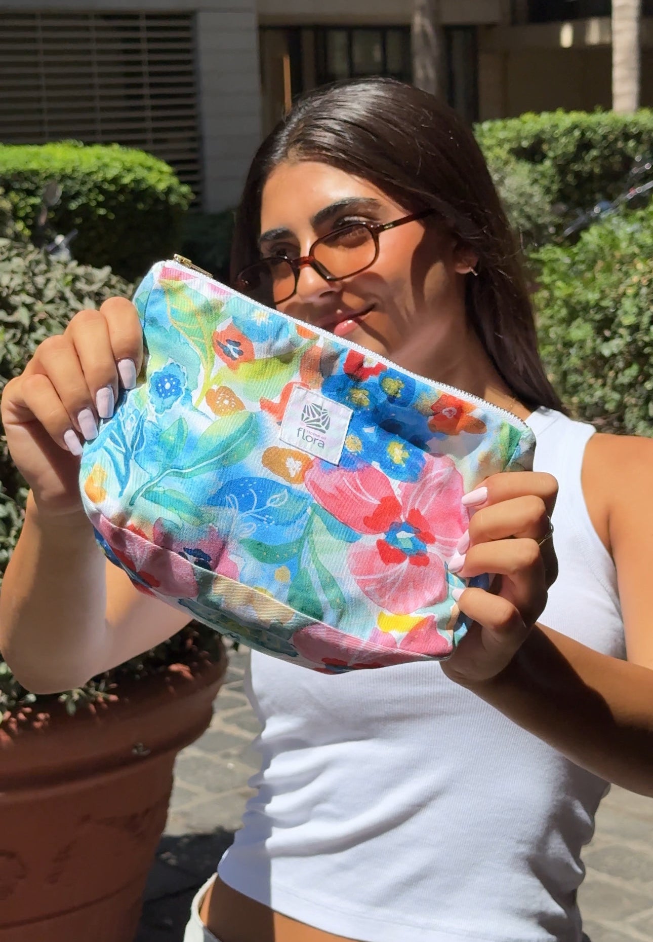 Woman holding a colorful floral-patterned pouch outdoors.