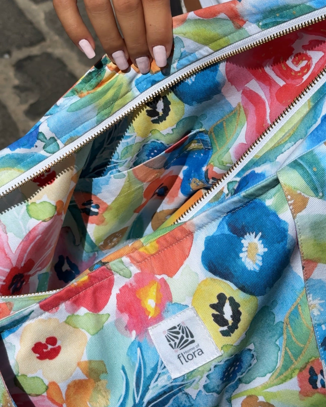 Colorful floral-patterned bag with a visible brand logo, held by a person.