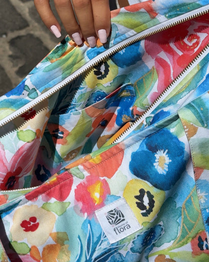 Colorful floral-patterned bag with a visible brand logo, held by a person.