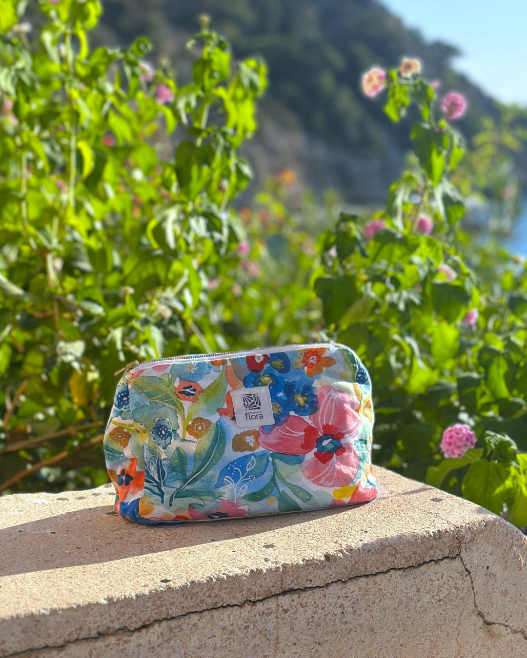 Floral patterned pouch on a stone ledge with greenery in the background
