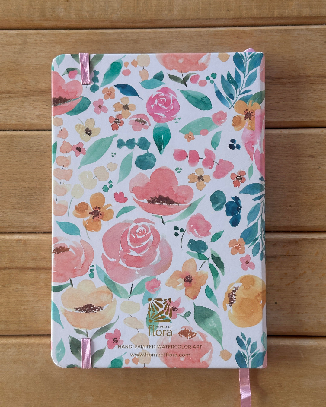 Floral notebook with pink ribbon on a wooden surface