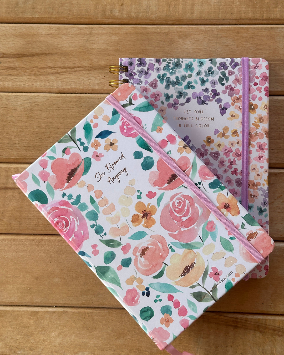 Two floral-patterned notebooks on a wooden surface