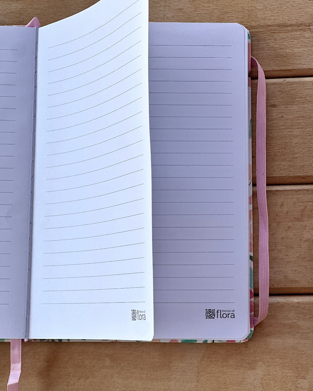 Open notebook with lined pages on a wooden surface, featuring the brand 'flora'.
